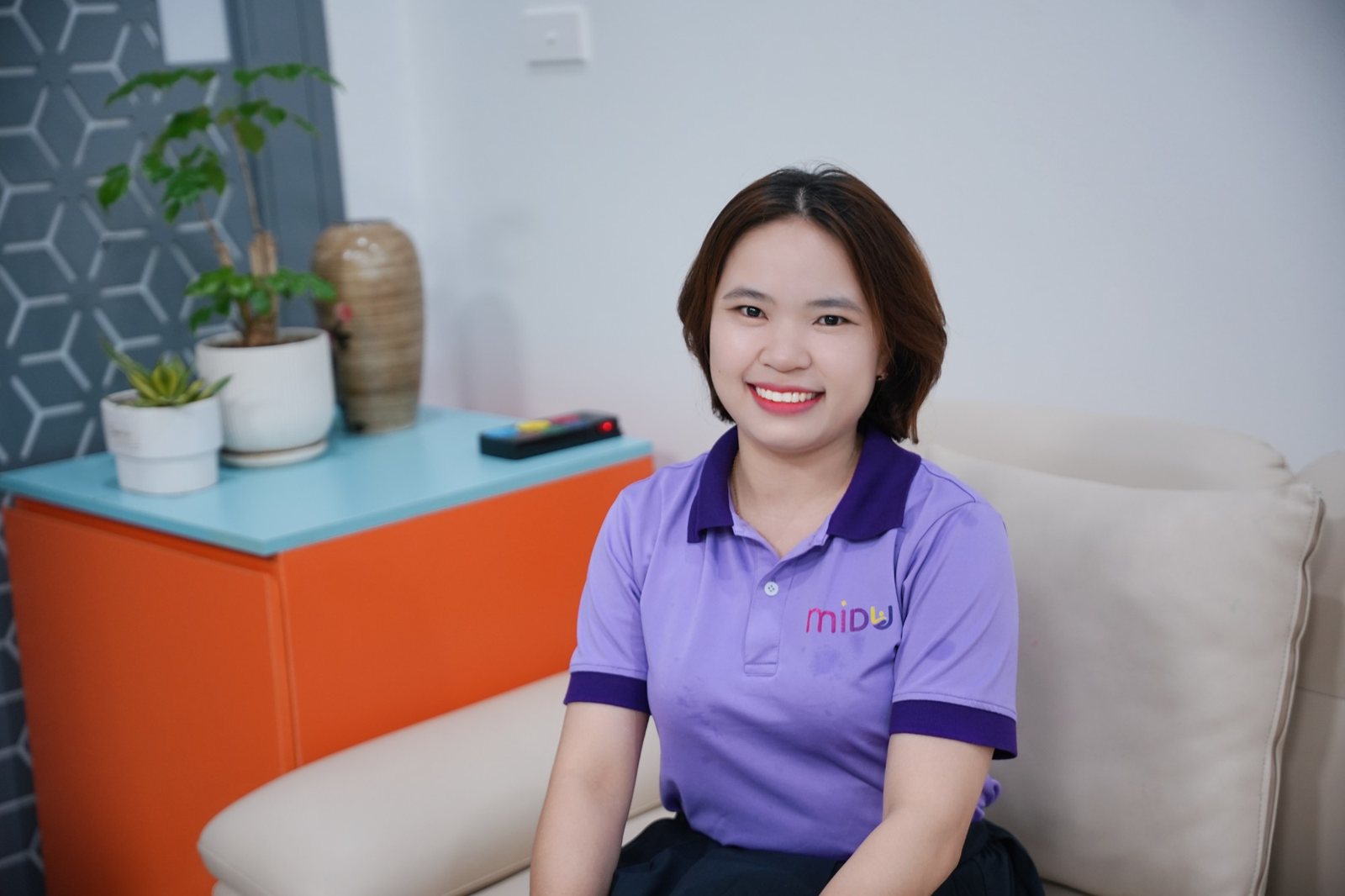Hoàng Gấm mặc áo Midu màu tím, ngồi cười trong phòng tư vấn
