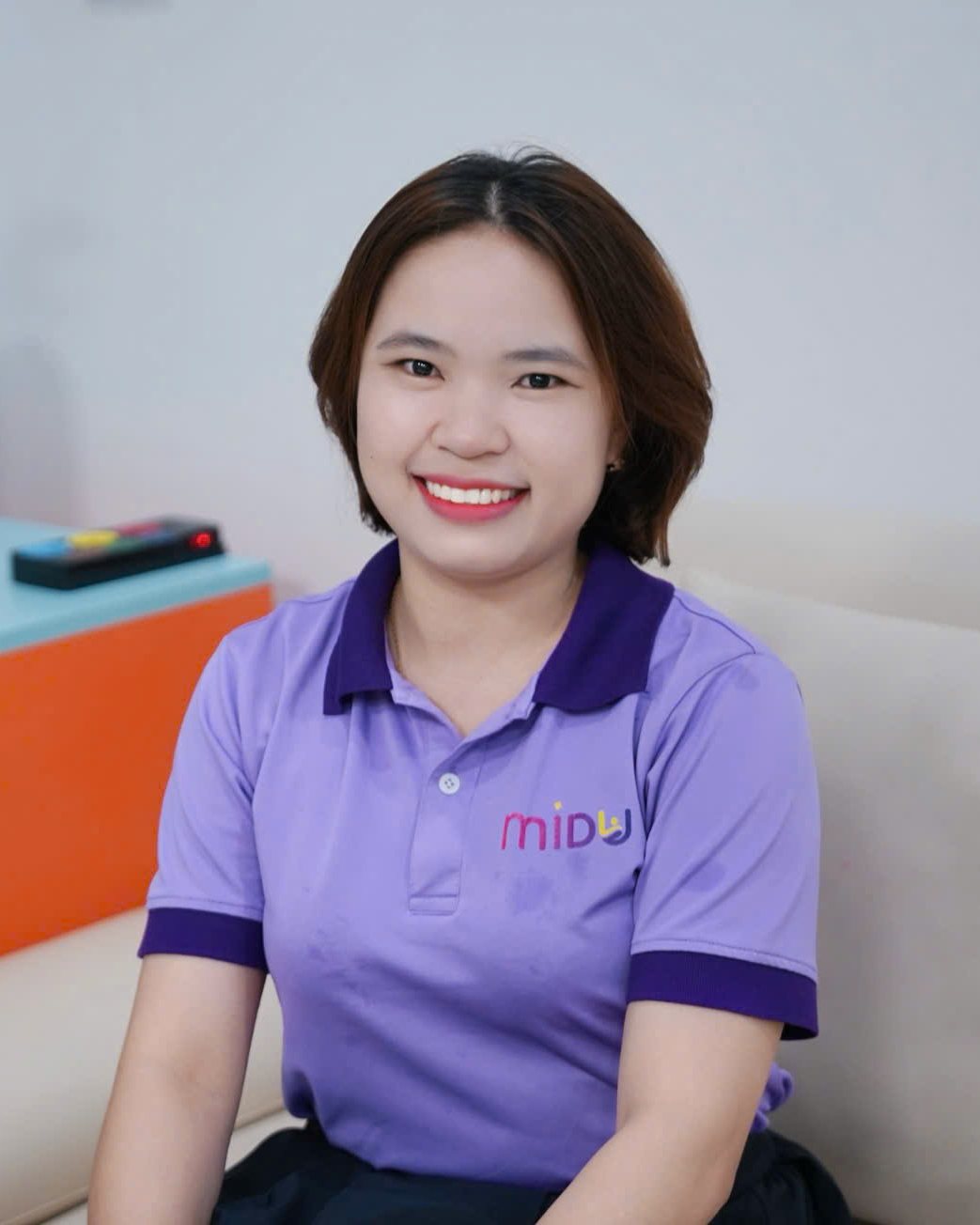Hoàng Gấm mặc áo Midu màu tím, ngồi cười trong phòng tư vấn